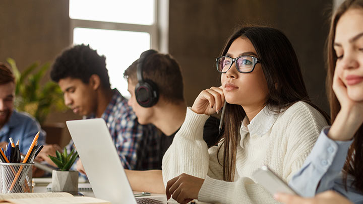 Photo of college students in a classroom using different technology. One of them is gazing at the distance wondering about their career and educational choices. Or so we hope.